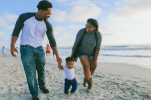 homme en chemise à manches longues rayée noire et blanche tenant un bébé en chemise blanche sur la plage