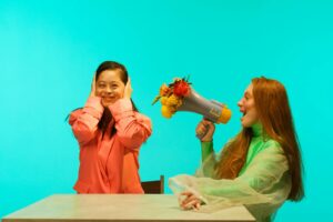 Deux femmes interagissant avec un mégaphone floral créatif sur un fond bleu vibrant.